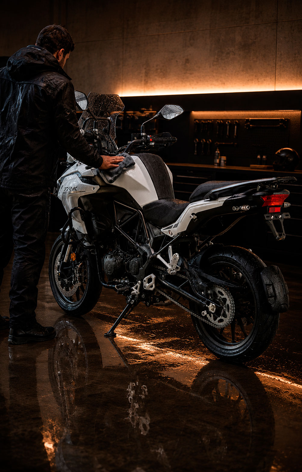 Persona seca y limpia una Benelli TRK 502 después de rodar bajo la lluvia, dentro de un taller con el piso mojado.